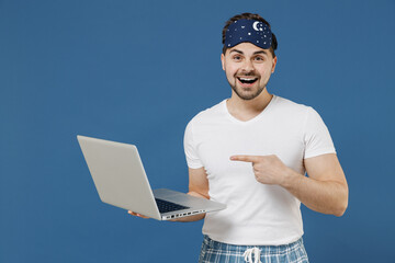 Young freelancer copywriter man in pajama sleep mask rest relax at home point index finger on...