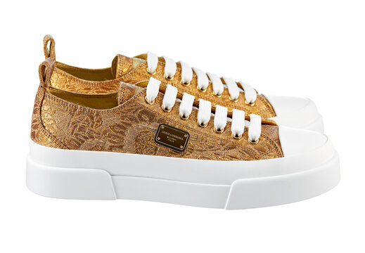 Fashionable dolce gabbana sneakers made of gold-colored fabric, with a logo, on a white sole, isolated on a white background. Side view. Belarus, Minsk, 02.06.2021.