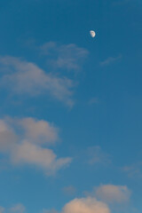 Blue sky with white gray clouds and bright white moon silhouette