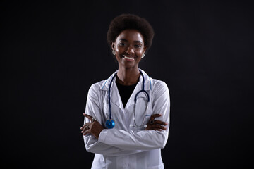 Black female doctor therapist smiling at black background. African american woman in medical gown with stethoscope standing crossed arms and smiling. - Powered by Adobe