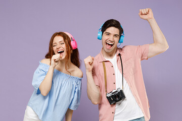 Two traveler tourist woman man couple in shirt headphones listen to music sing in microphone at karaoke club isolated on purple background Passenger travel abroad weekends getaway Air flight concept.