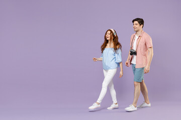 Naklejka premium Full length side view two happy traveler tourist woman man 20s couple in summer clothes wlak go isolated on purple background. Passenger travel abroad on weekends getaway. Air flight journey concept.