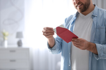 Man holding envelope with greeting card at home, closeup