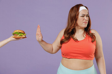 Young sad chubby overweight plus size big fat fit woman in red top warm up training do stop palm hand gesture refuse fastfood burger isolated on purple background gym Workout sport motivation concept