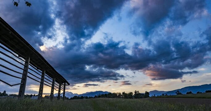 Time lapse of beautiful and dramatic sunset over grassland farming field and Alps mountains in the distance. Wooden hayrack decorating the field in Slovenia. Wide angle, static shot