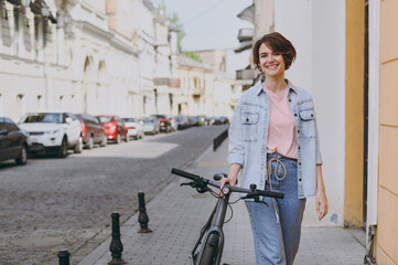 Young smiling happy pedestrian caucasian woman 20s wearing casual jeans clothes eyeglasses strolling walk go down city street outdoors with bicycle bike People youth active urban lifestyle concept