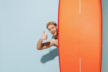 Handsome young blond man in swimsuit relax near hotel pool hiding cover with orange sup board show...