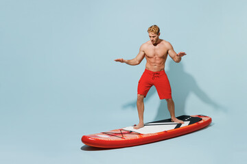 Full length young sexy sporty fun strong man 20s wear red shorts swimsuit relax stand on orange sup...