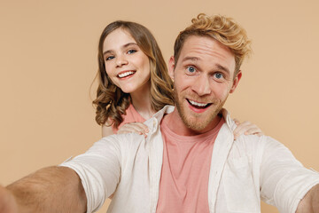 Close up smiling young parent man have fun with child teen girl wear casual pastel clothes Daddy little kid daughter do selfie shot on mobile phone stand behind father isolated on beige background