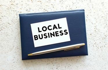 Text LOCAL BUSINESS on a business card lying on a blue notebook next to the pen.