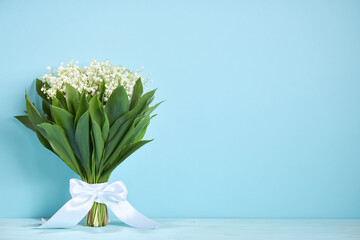 Bouquet of lilies of the valley with a white ribbon on a blue background. Postcard concept. Copy spase.