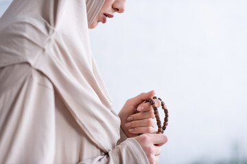 partial view of young arabian woman holding rosary during pray at home