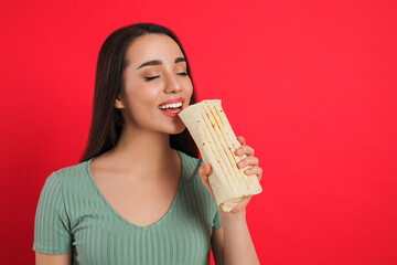 Young woman eating tasty shawarma on red background. Space for text