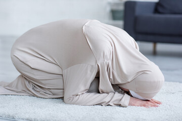 muslim woman in traditional clothing praying on floor at home