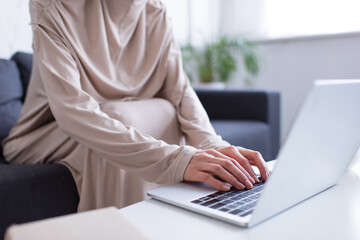 cropped view of muslim woman typing on laptop on blurred foreground