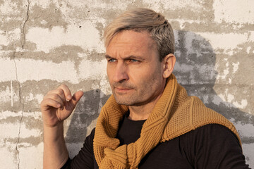 Pensive stylish charming blond middle-aged man of model appearance in front of a white brick wall....
