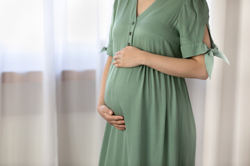 Close up cropped of pregnant woman in green dress touching caressing belly, expecting first baby child, feeling bumps, beautiful young future mom enjoying healthy pregnancy, motherhood concept