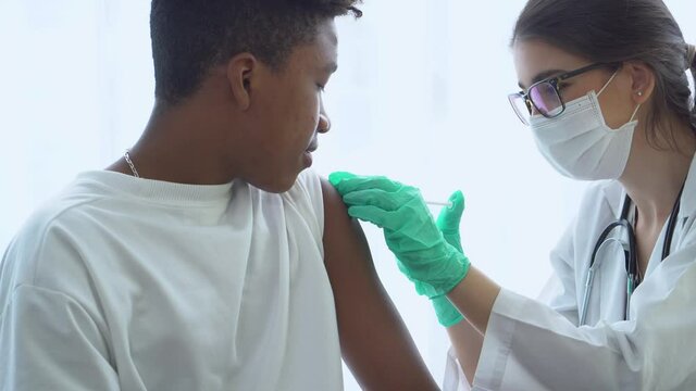 African American teenage boy vaccinated to prevent coronavirus or COVID-19 Caucasian female doctor.