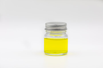 Glass jar containing with silver lid and  yellow oil  display on white background.