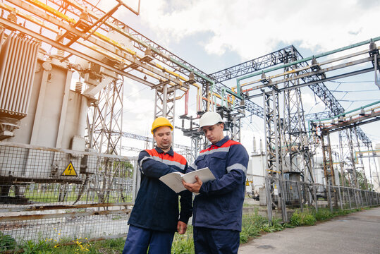 Two specialist electrical substation engineers inspect modern high-voltage equipment in the evening. Energy. Industry