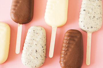 Line of milk and white chocolate popsicles on light pink background, top view