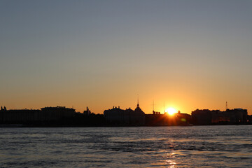 Naklejka premium silhouette of flying birds over the river against the background of city buildings during sunset