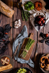 Flat lay dark photography of asparagus, bread, tomatoes,garlic and plums on a table of old wood. Vegetables recipe of for autumn or winter. Moody top view of seasonal products on a wooden table.