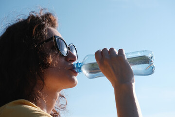Girl with glasses drinks water from a bottle in hot weather.