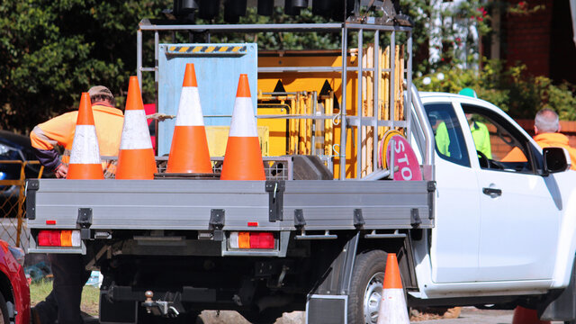 Road work company ute loaded with signs and orange road cones. Road workers are in the background