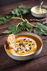Food photography of a vegan cream soups on a table of old wood. Vegetables recipe of a creamy soup with selective focus. Puree of seasonal products on a wooden board among fig leaves