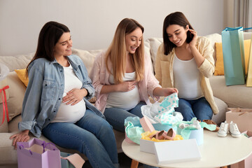 Happy pregnant women spending time together in living room after shopping