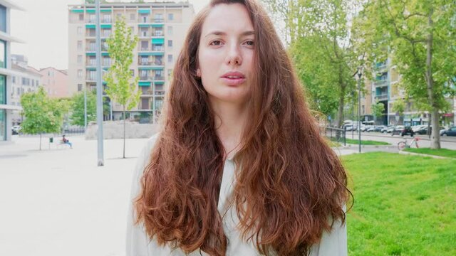 Woman with long hair standing in city, staring at camera
