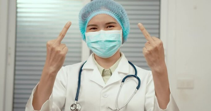 Doctor woman shows the middle finger. Bad expression. Hand gesture Fuck you. Rude attitude. Doctor's face in a protective mask and cap of a surgeon. Not a polite employee.