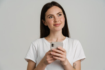 Young brunette woman in t-shirt smiling while using mobile phone