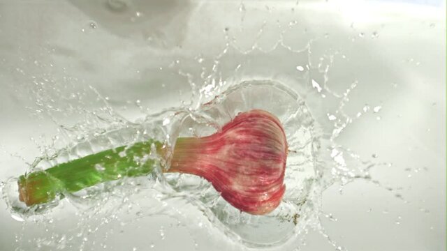 Super slow motion garlic falls into the ode with splashes on a white background. Filmed on a high-speed camera at 1000 fps. High quality FullHD footage