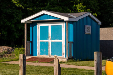 Weathered blue and white shed at sunset. Ramp in front. Peeling paint on shed, wooden posts in foreground.