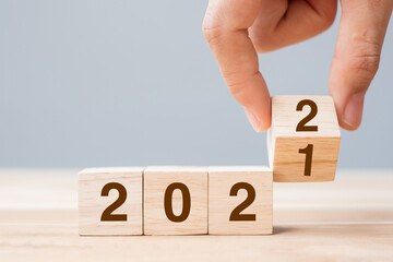 Businessman hand holding wooden cube with flip over block 2021 to 2022 text on table background....