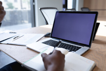 Mid section of businessman with laptop taking notes while sitting in meeting room at modern office