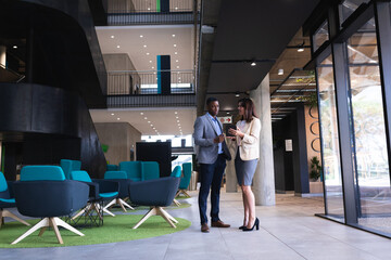 Diverse businessman and businesswoman discussing over digital tablet at modern office
