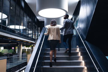 Rear view of diverse businessman and businesswoman climbing up the stairs at modern office