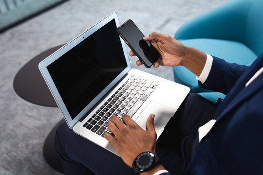 Mid section of african american businessman using laptop and smartphone at modern office