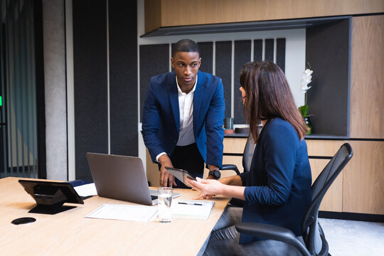 Diverse businessman and businesswoman discussing over digital tablet in meeting room at office