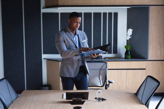 African american businessman reading documents while standing in meeting room at modern office