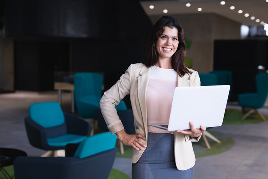 Portrait of caucasian businesswoman holding a laptop smiling while standing at modern office