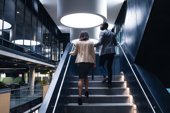 Rear view of diverse businessman and businesswoman climbing up the stairs at modern office