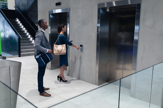 Caucasian businesswoman holding smartphone pressing the lift button at modern office