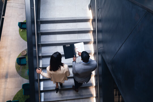 Diverse businessman and businesswoman discussing together standing on the stairs at office