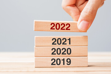 hand pulling 2022 block over 2021, 2020 and 2019 wooden building on table background. Business...