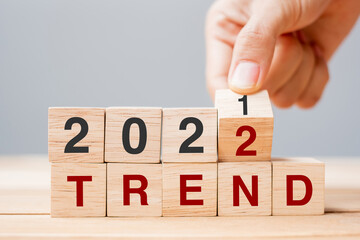 Businessman hand holding wooden cube and flip over block 2021 to 2022 TREND on table background....
