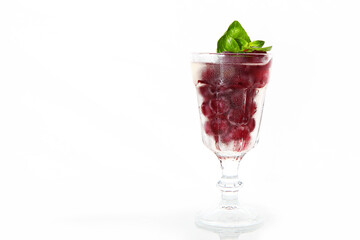 Red berry with basil leaves in a glass glass. Basil leaves. Cherry lemonade in a transparent glass. Refreshing drink. Copy space. White background.